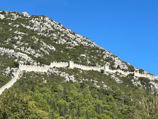       Long stone wall along a mountain slope.
  