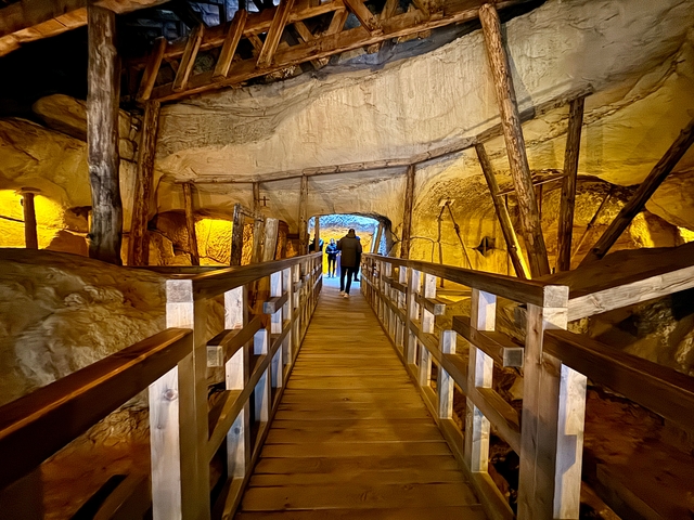 People walking over a wooden bridge inside a cave-like structure.