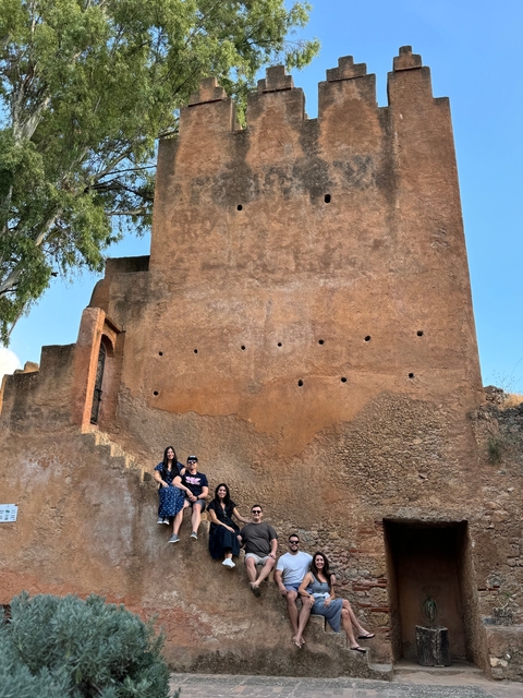       Group of people sitting outside a historic building.
  