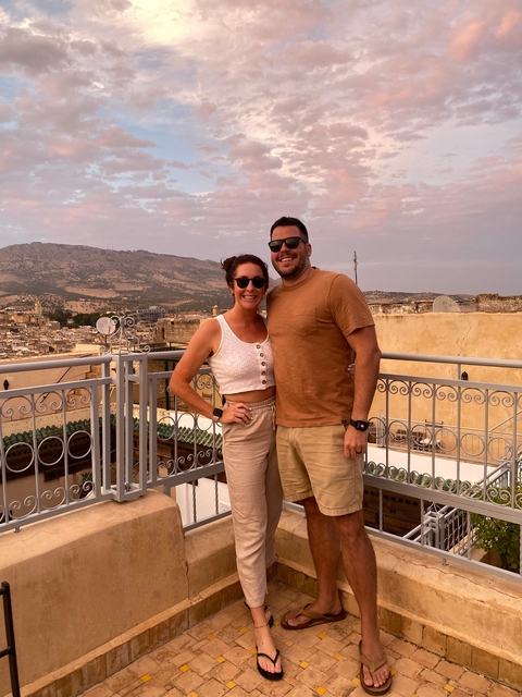 Couple posing on a balcony with a cityscape view.