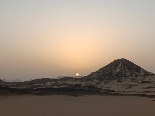       Desert landscape with a mountain and the sun setting.
  
