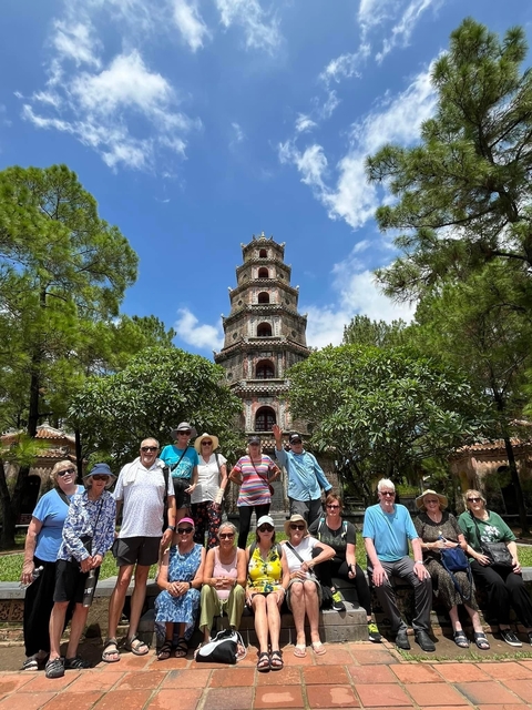       A group of tourists posing in front of a historic pagoda surrounded by trees.
  