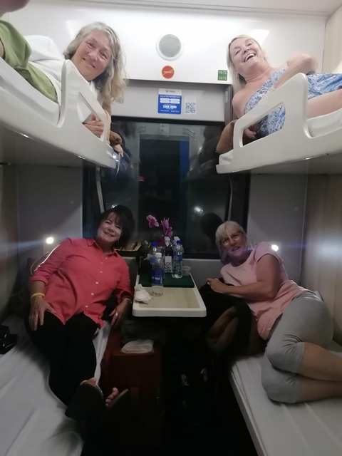       Two women sitting inside a train compartment, smiling.
  