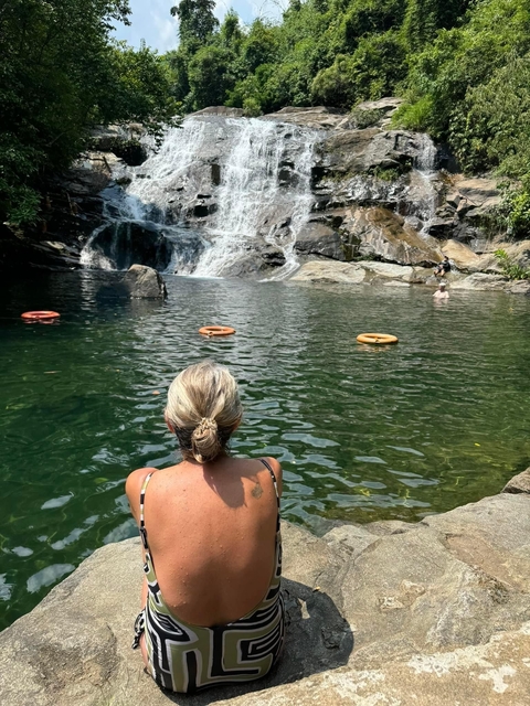       A woman sitting by a serene natural pool with a waterfall.
  