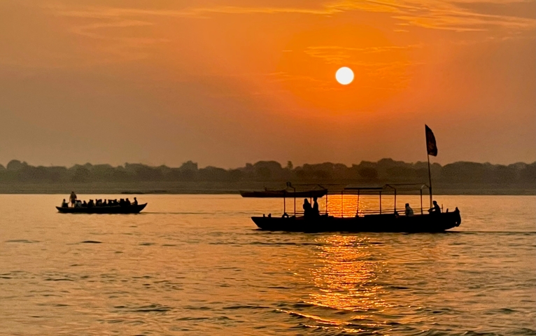       Row boats on a river at sunset with a glowing sky.
  