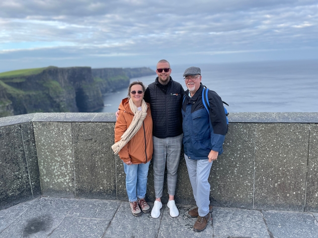 Three people standing on a cliff overlooking the ocean