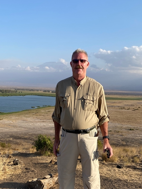       Man standing in a natural landscape with mountains.
  