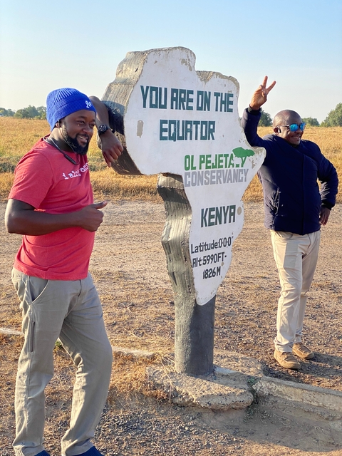       Two men posing with a sign at the equator.
  