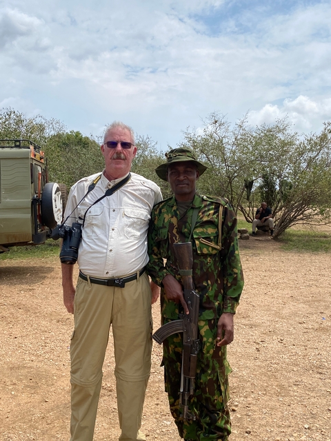       Two men posing in a bush setting, one in camouflage.
  