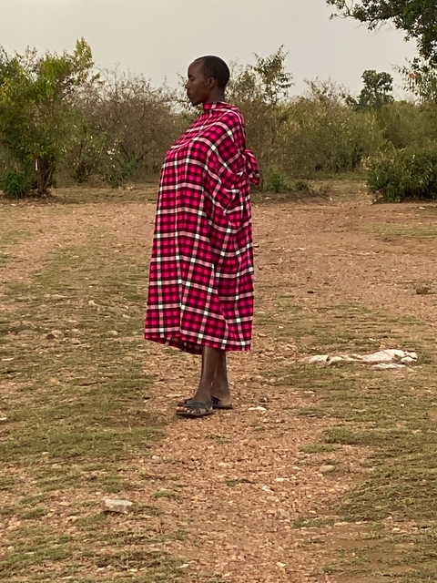       Person in traditional red and black checked wrap outdoors.
  