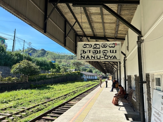       Railway platform with traditional signage and people waiting.
  