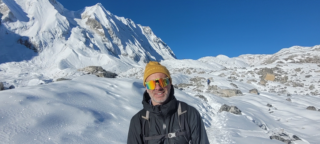       Man in winter gear standing against a snowy mountain backdrop.
  