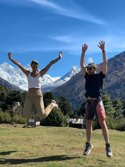 Two people jumping with snow-capped mountains in the background.