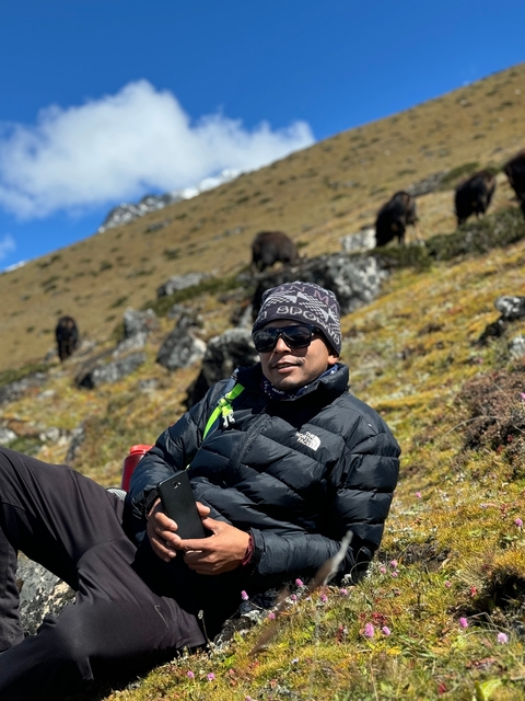       Man resting on grassy hillside with mountains in the distance.
  