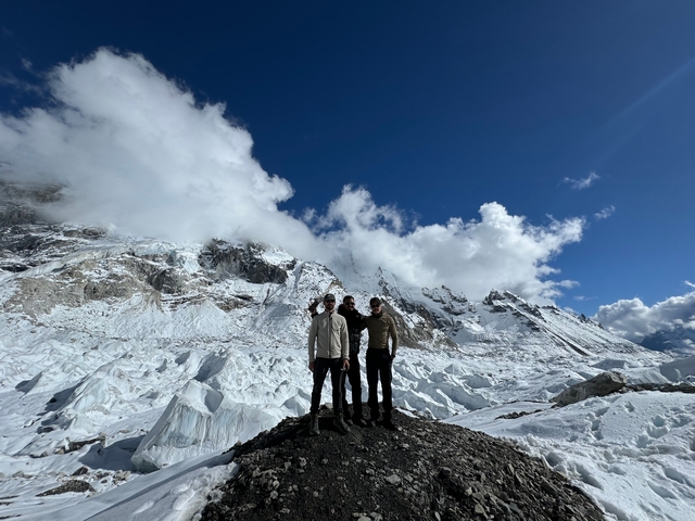       Three people standing on a mountain summit with snow-covered peaks.
  