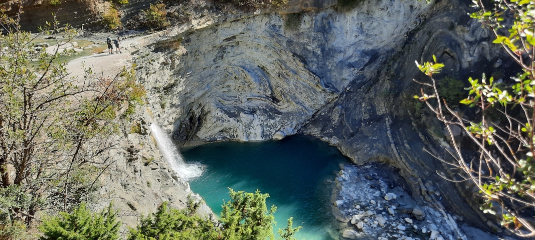       Waterfall and a blue water pool amidst rocky terrain.
  