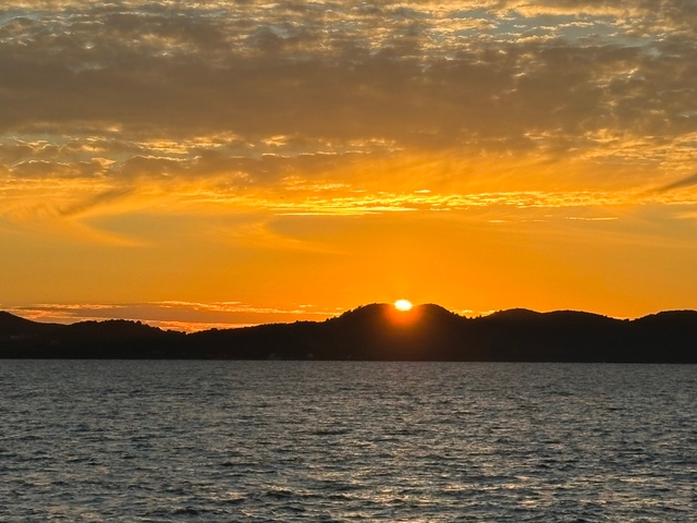       Sunset over the sea with hills silhouetted.
  