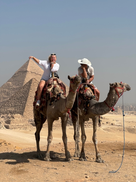 Two people on camels in front of pyramids.