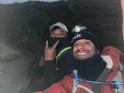 Two people smiling, one wearing a headlamp in a dim environment.