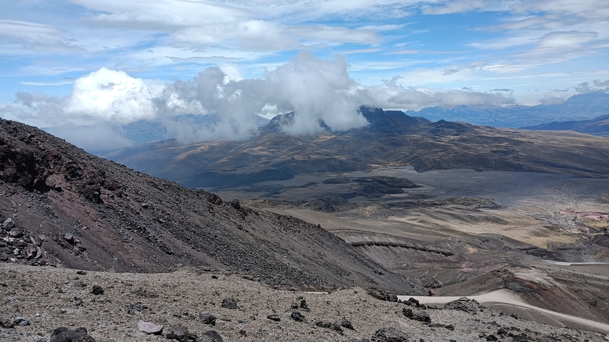 A vast landscape with rocky terrain and clouds over a mountain.