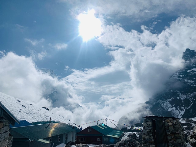       Mountain view with snow and clouds under a bright sun.
  