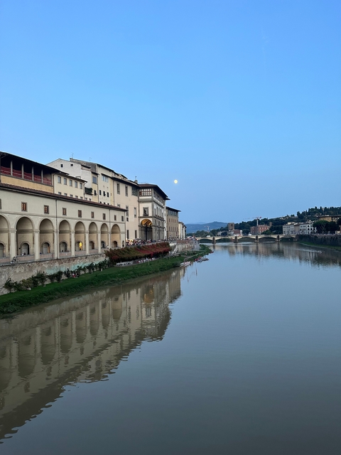       River view with historical buildings and a moon in Florence.
  
