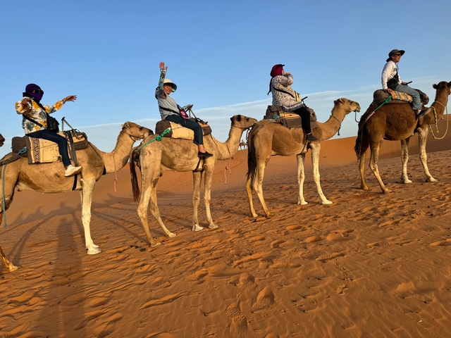 Group of people riding camels in the desert at sunset.