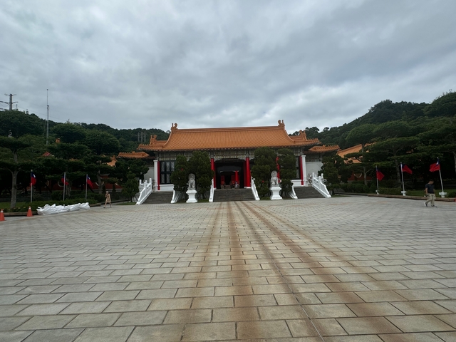 Traditional Taiwanese building with red roof and flags, surrounded by trees.