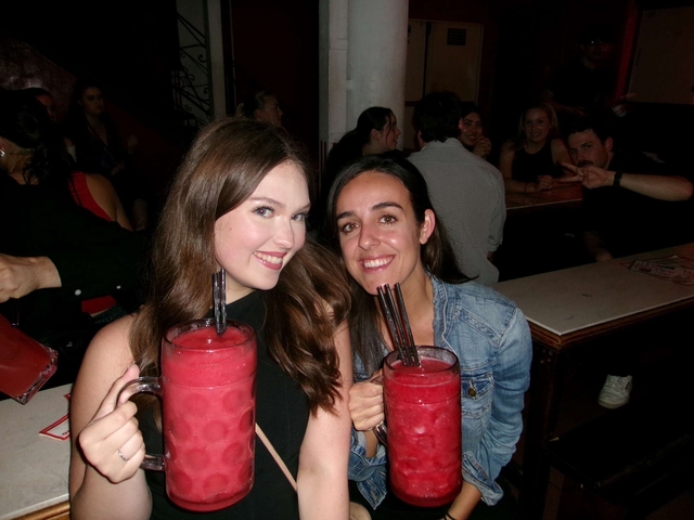 Two women holding large drinks in a bar setting.