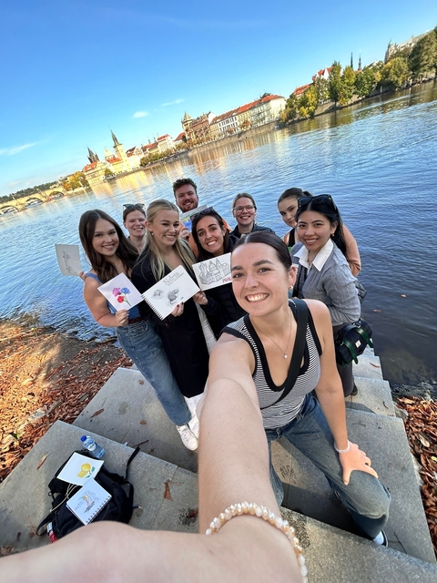 Group of friends smiling and holding drawings by a river.