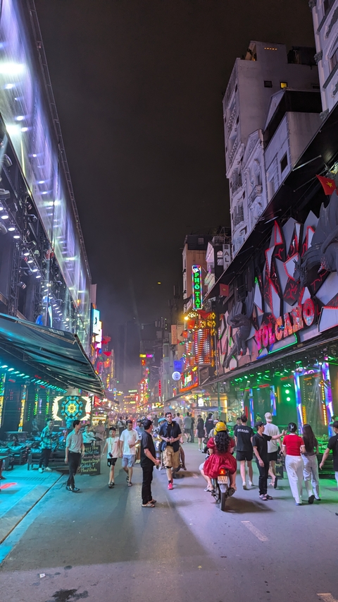       Busy street at night with neon signs and many people.
  