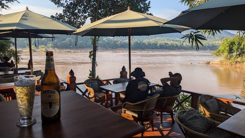       Bar terrace overlooking a river with people enjoying drinks.
  