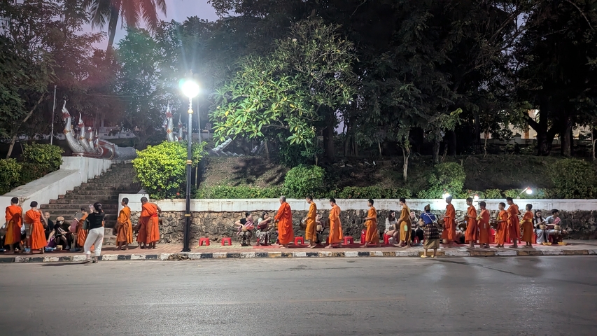      Monks in traditional robes walking down a street at dawn.
  