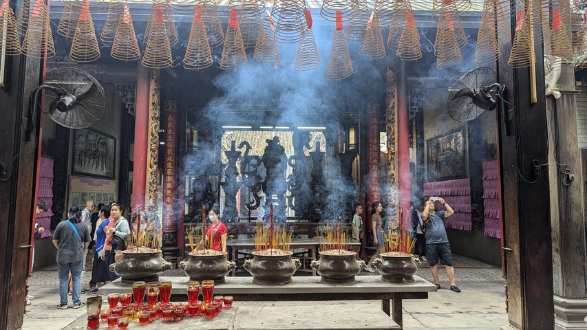 Inside a temple with incense burning and people observing.
