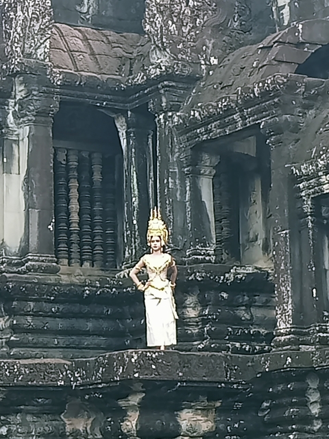       Person dressed in traditional attire in front of ancient stone structures.
  