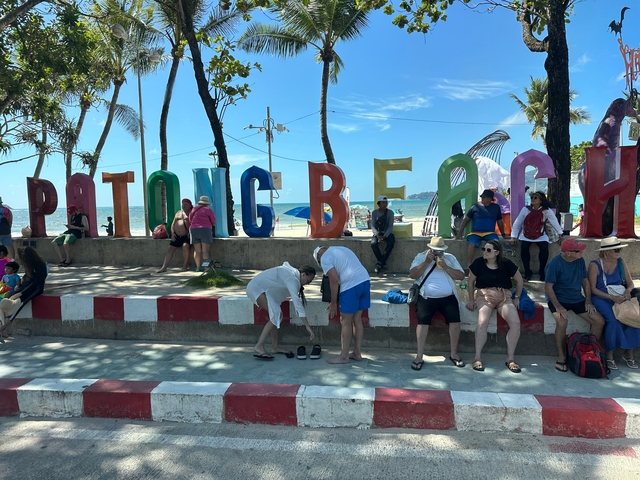 Patong Beach sign with people sitting and walking around.