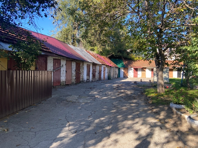       Row of rustic garages or small storage units in a shaded area with trees.
  