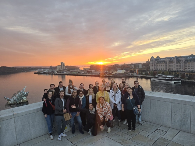       Group of people posing with a cityscape and sunset.
  