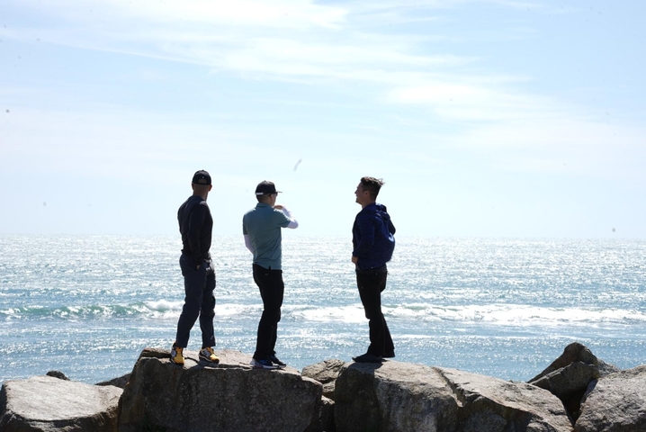       Three people standing on rocks by the ocean during the day.
  