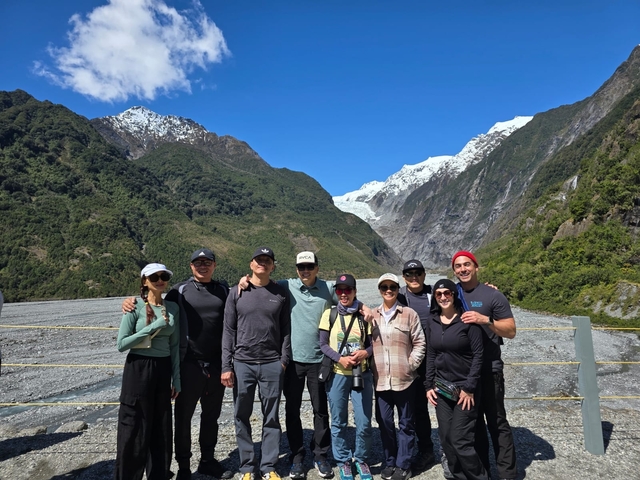       Group of people posing in front of a glacier with mountains in the background.
  