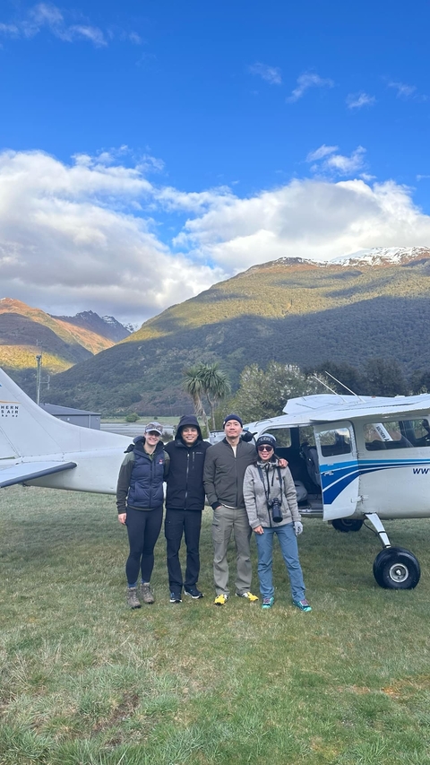       Four people standing in front of a small airplane with mountain scenery in the background.
  