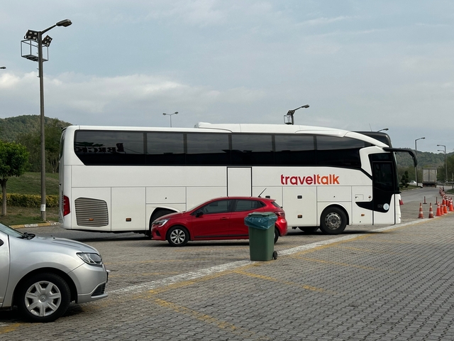 Parked tour bus with brand name 'Traveltalk' and a red car.