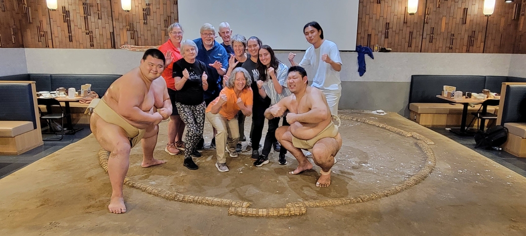 Group of people posing with sumo wrestlers indoors.