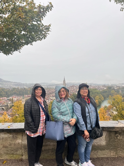       Three people in jackets with a view of a city and river in the background.
  
