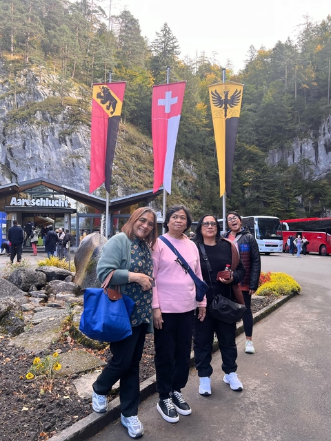 Four people posing under flags in front of a tourist entrance.