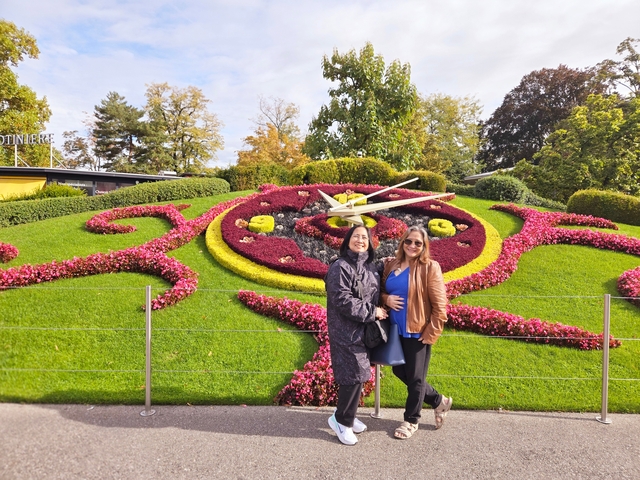       Two people posing in front of a floral clock in a city park.
  