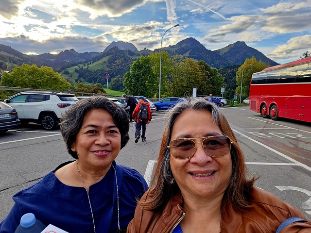       Two people smiling with a scenic mountainous background and a red bus.
  