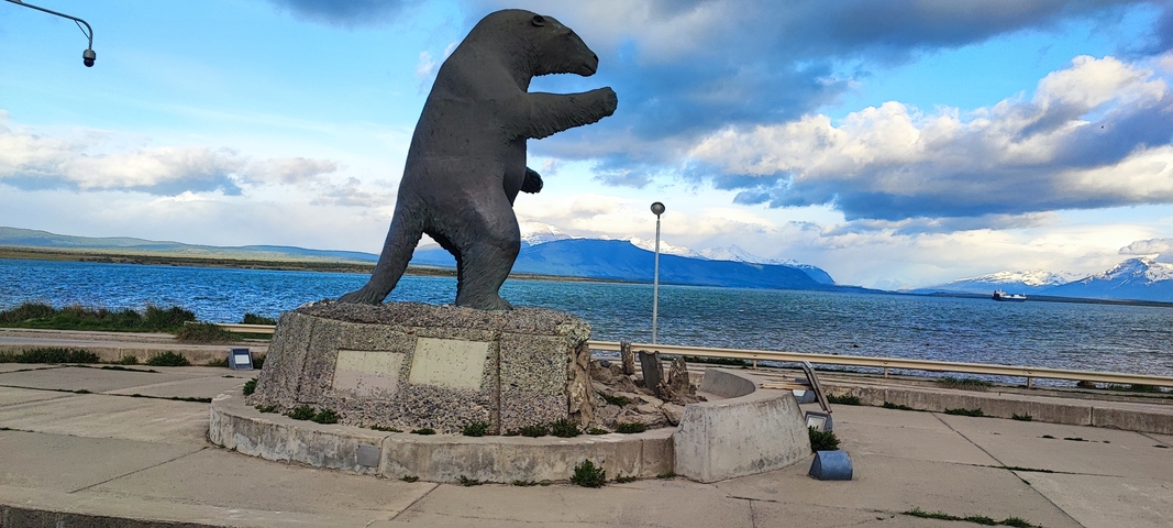       Statue of a bear in a waterfront area with mountains in the distance.
  