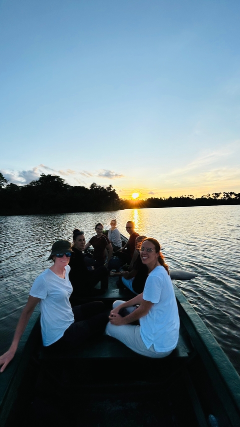 Group of people in a boat on a river at sunset.