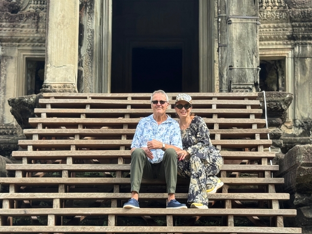       Two people sitting on steps in front of an ancient temple.
  